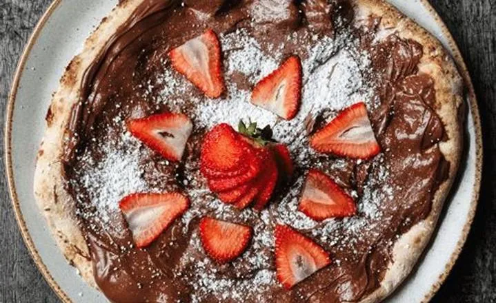Dessert pizza with chocolate hazelnut spread, strawberries and icing sugar